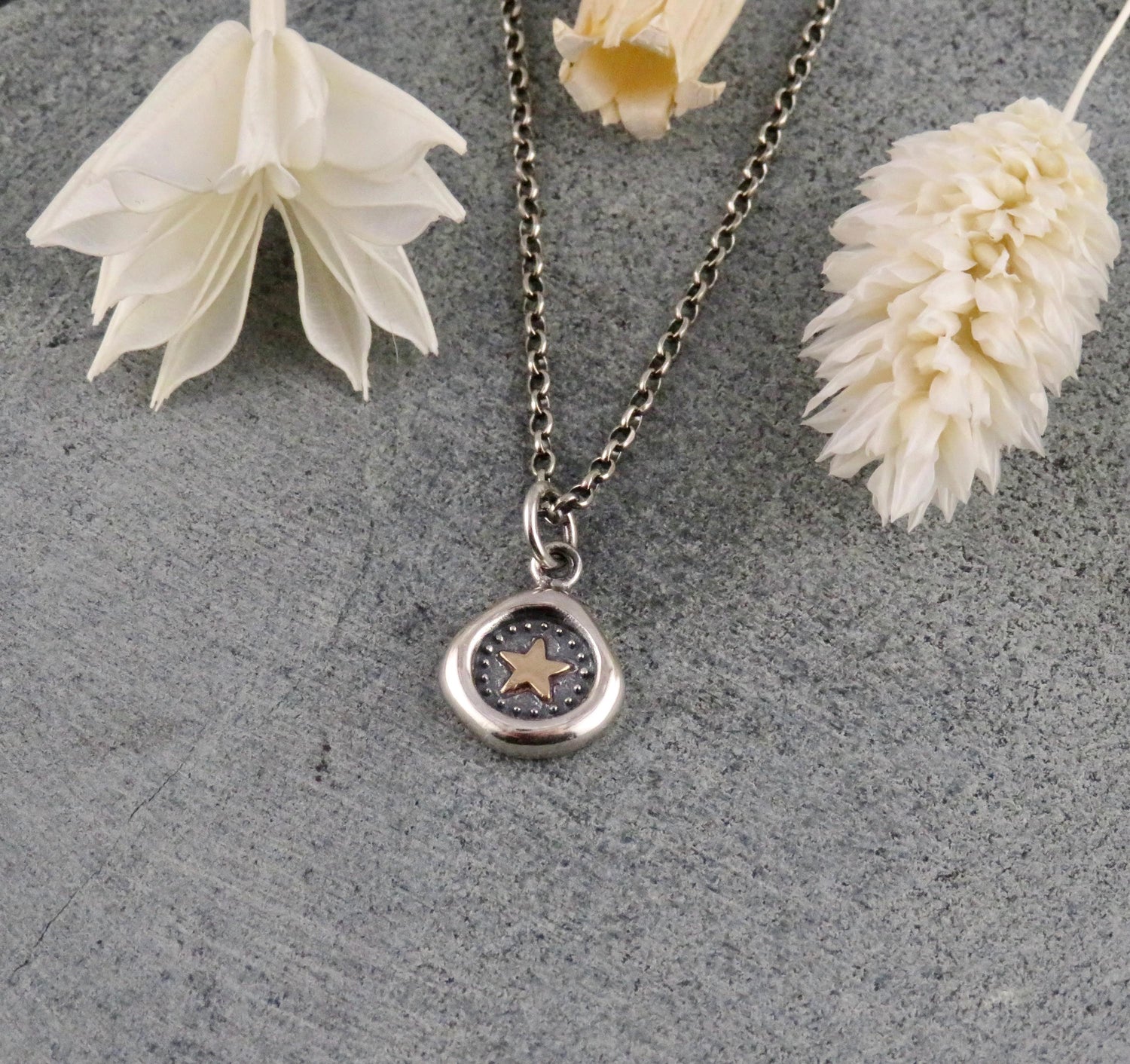 Silver necklace with a pendant on a gray surface with white flowers.